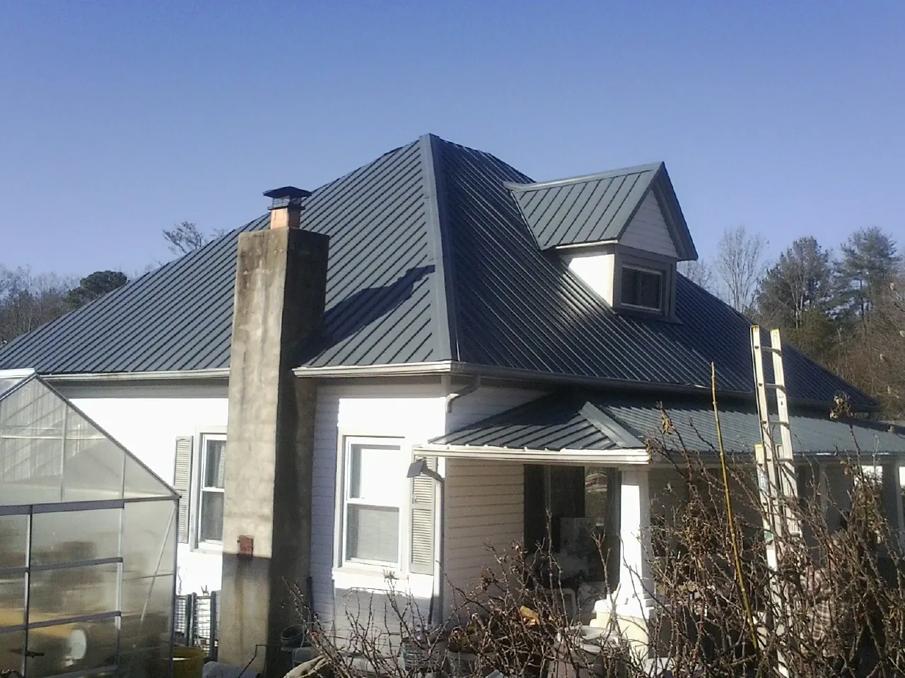 Dark blue standing seam metal roof on a white farmhouse with dormer — Slate & Tile Roof Repair by Roofing Brothers in Gillsville