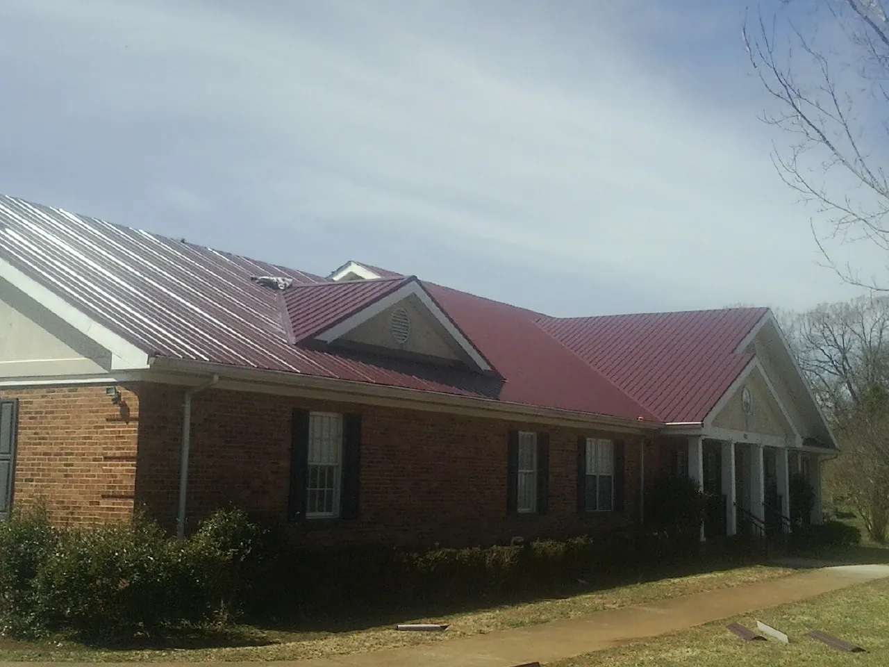 Red metal roof with gabled entries on a long brick building, from a Hail Damage Roof Repair job in Gillsville