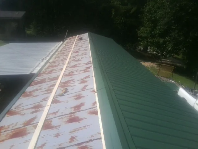 Old rusted panels beside newly installed green metal roofing — Wind Damage Roof Repair by Roofing Brothers in Gillsville