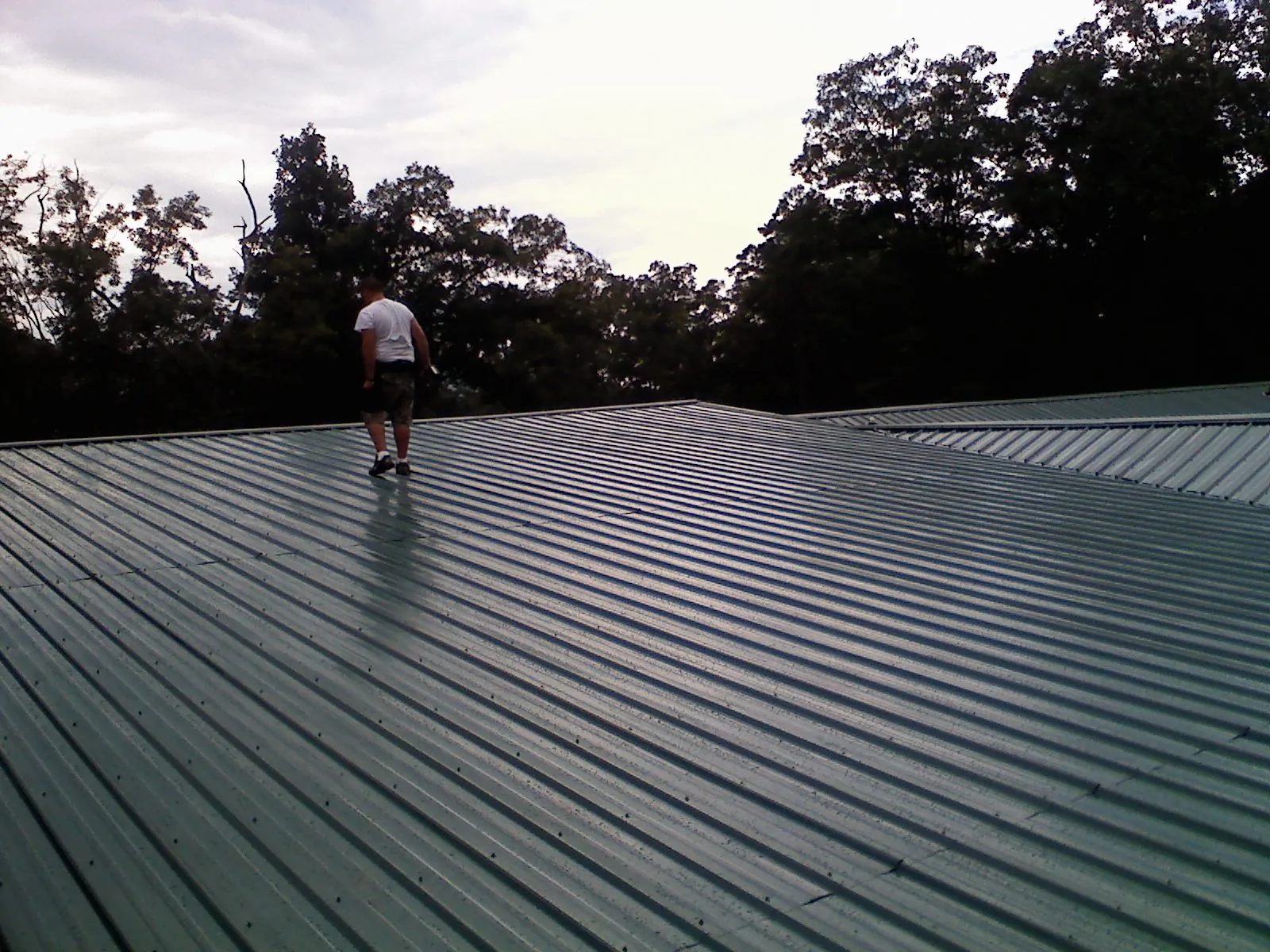 Roofer walking a wide expanse of new green metal roofing in Gillsville
