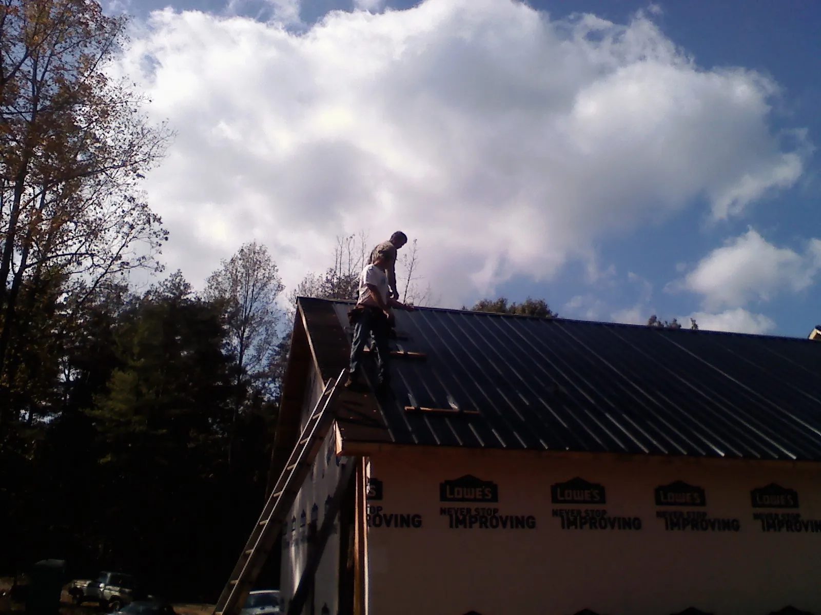 Roofer fastening dark metal panels high against a cloudy sky, from a Roof Inspection job in Gillsville