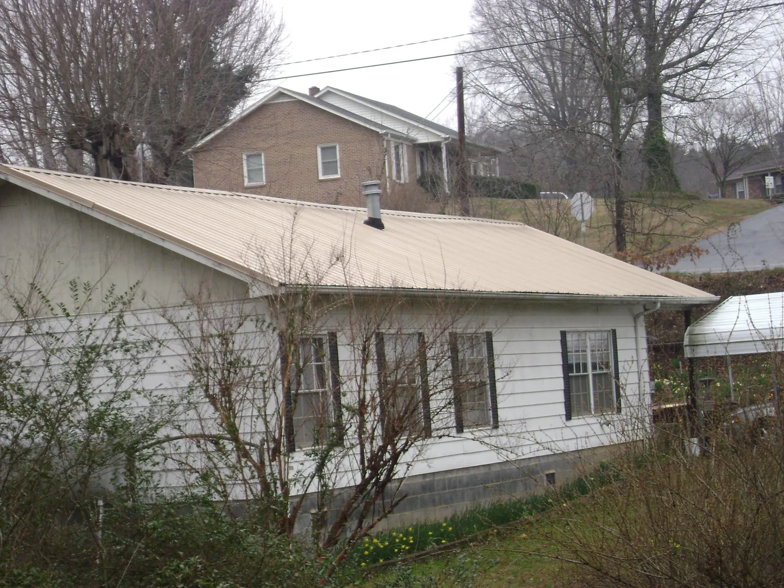 Tan metal roof on a white sided house set into a hillside — Commercial Roofing by Roofing Brothers in Gillsville