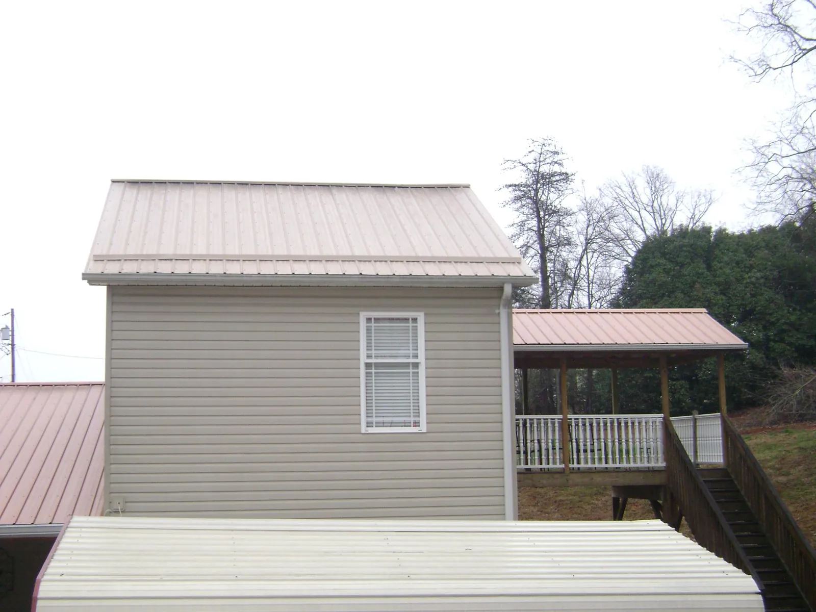 Tan metal roofs on a two story addition and attached porch, from a Roof Replacement job in Gillsville